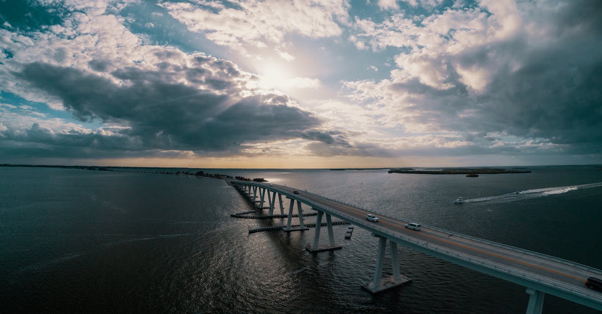 Dramatic aerial shot of a long bridge over a vast body of water under cloudy skies.