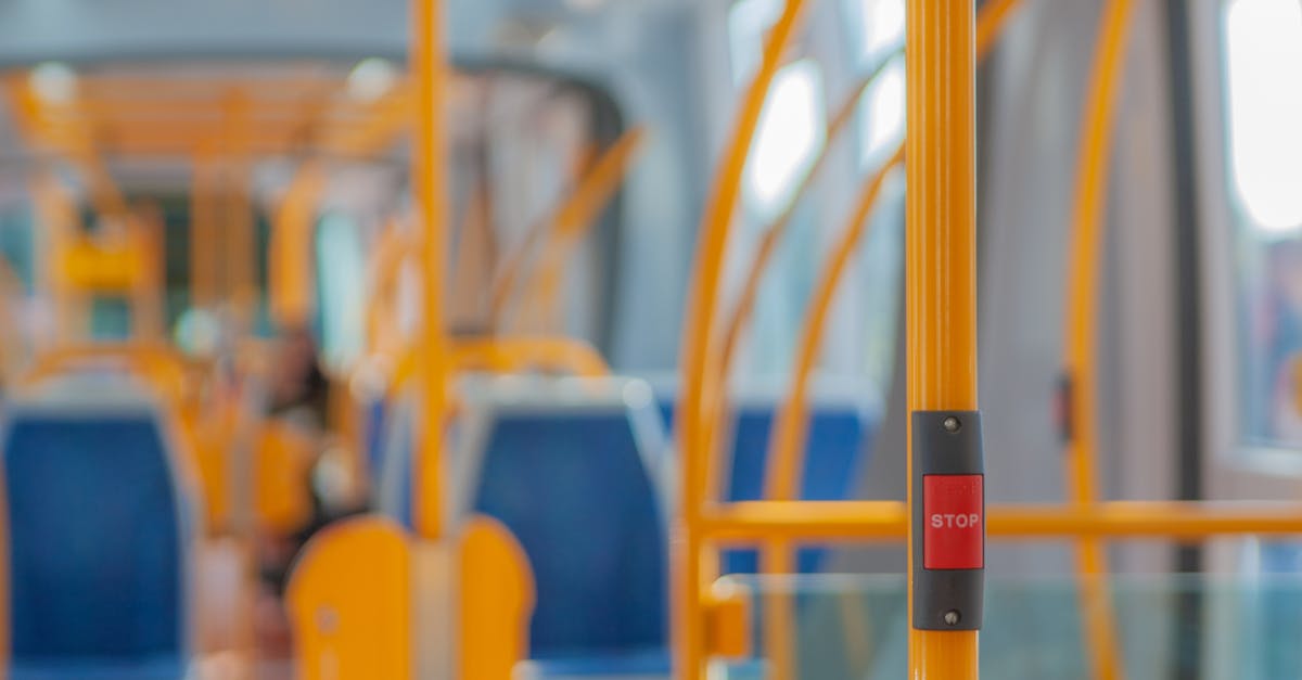 Red stop button on yellow handrail in modern empty public bus during daytime