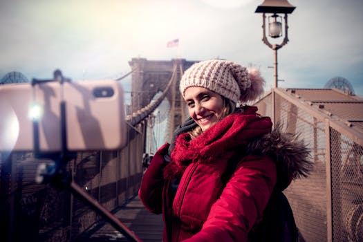 A woman wearing winter attire takes a selfie on the Brooklyn Bridge in New York City.