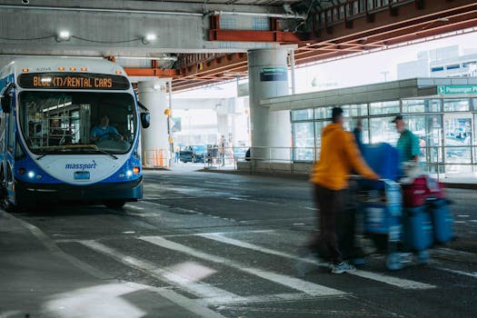 Busy airport scene showing travelers in motion and a rental car bus waiting under a covered terminal.